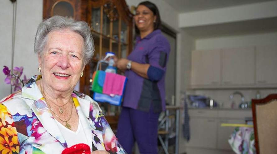 Oudere vrouw lacht in de camera met een lachende medewerkster op de achtergrond