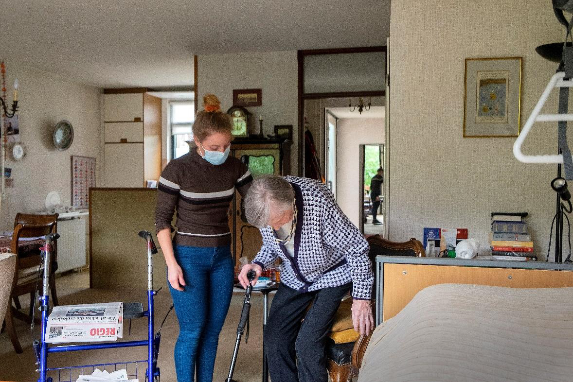 Jonge wijkverpleegkundige helpt een oudere dame in haar stoel