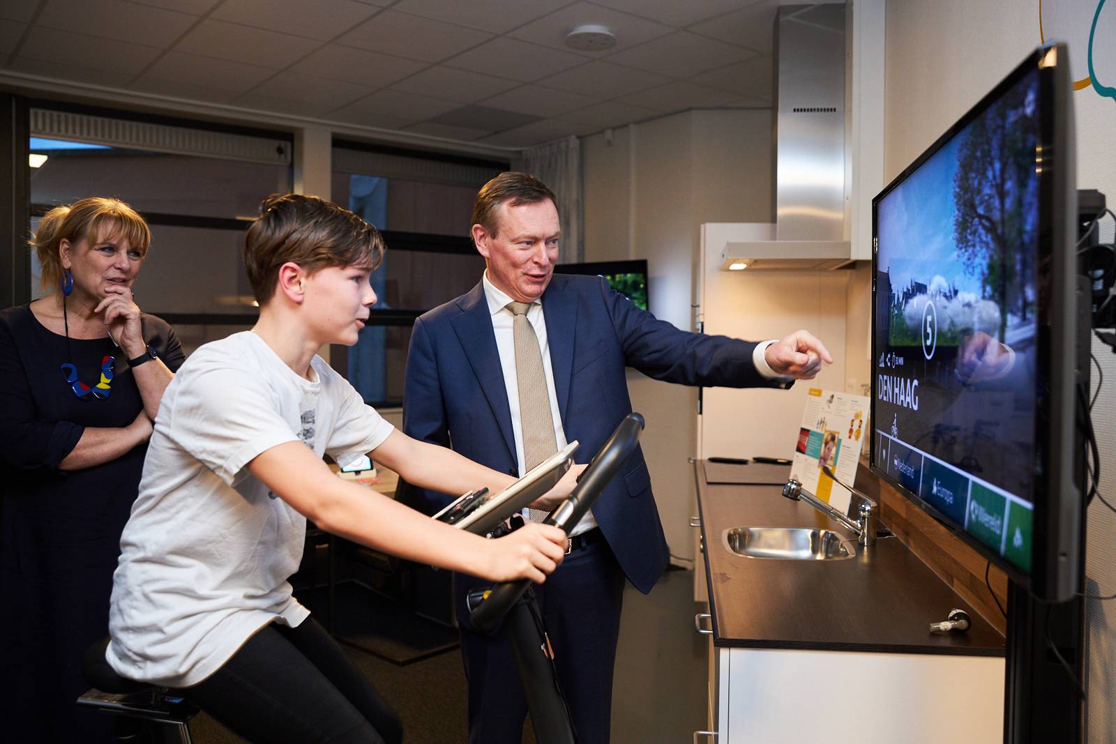 Minister Bruins bekijkt samen met een jongeman de simulatie op de fiets