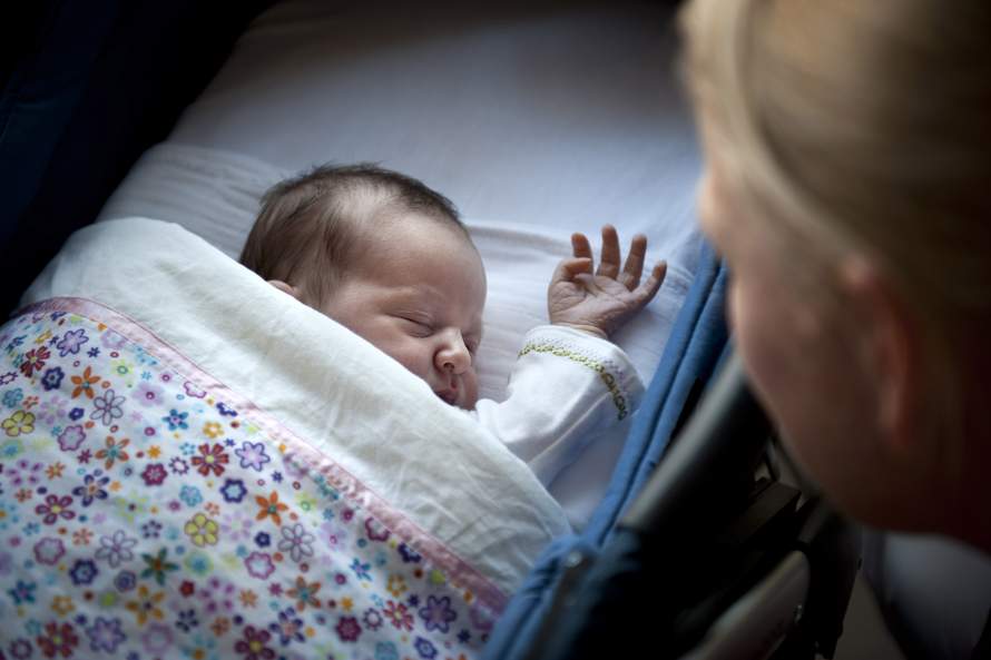 Kraamverzorgster kijkt bij een slapende pasgeboren baby