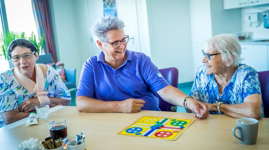 Verpleegkundige zit aan tafel met oudere patiënten