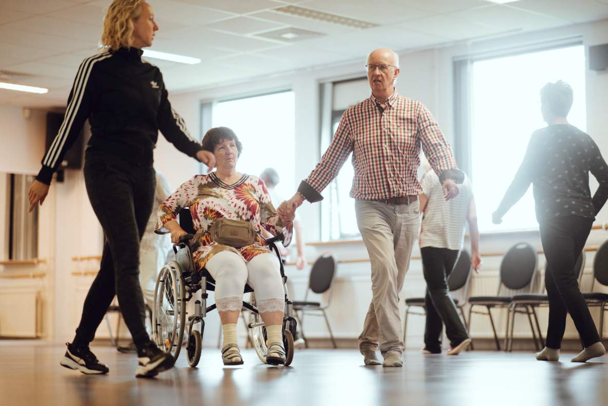 Een vrouw in rolstoel en haar partner volgen de instructies van een dansdocente.