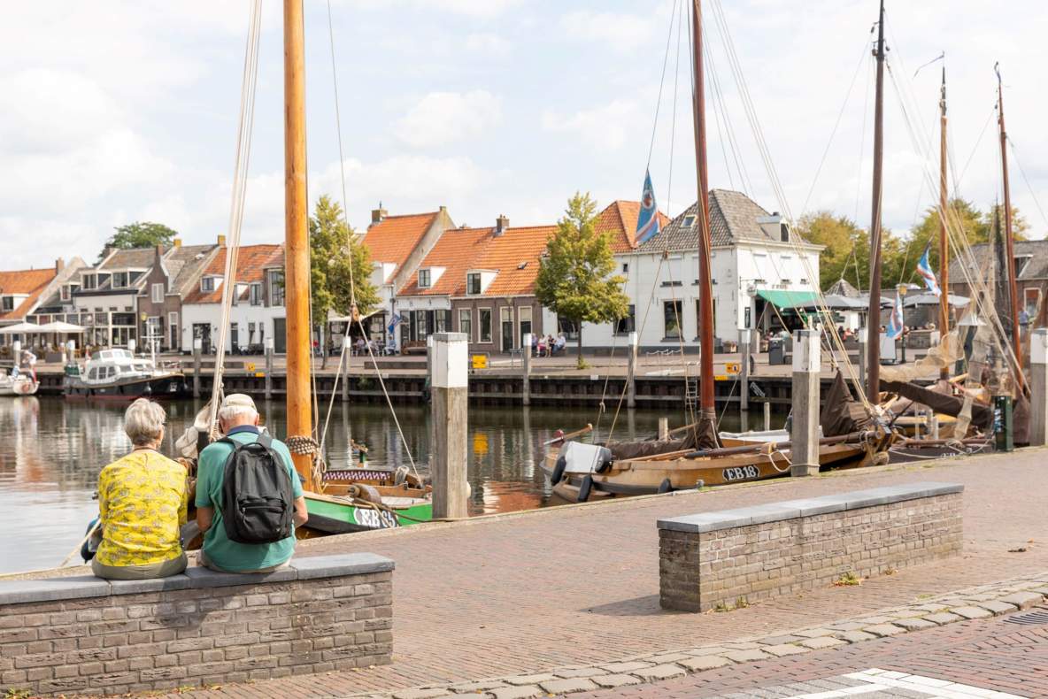 Foto van een haventje en twee oudere mensen die op een muurtje zitten.