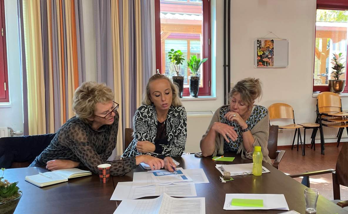 Drie vrouwen vergaderen aan een tafel en kijken naar verschillende papieren op tafel