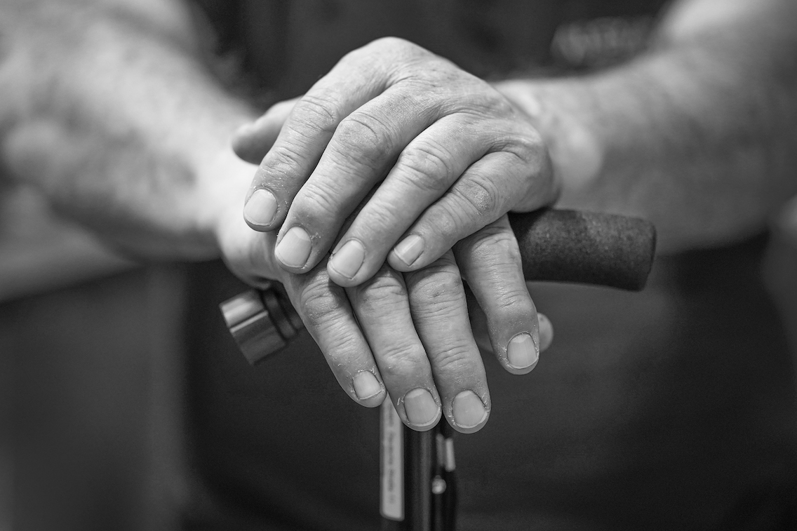 Handen van een oudere man leunend op een wandelstok
