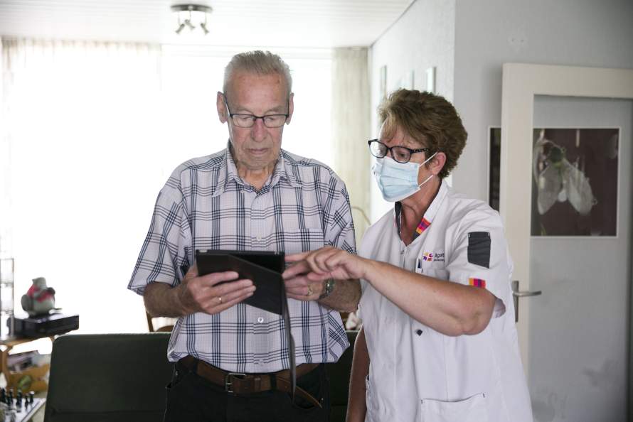 Wijkverpleegkundige geeft oudere client uitleg over een tablet.