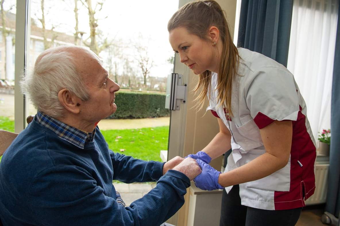 Verpleegkundige houdt handen van patiënt vast in de thuisomgeving