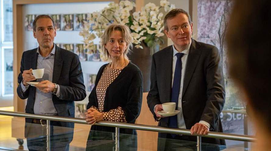 Bruno Bruins staat naast twee andere aanwezigen en kijkt blij richting presentator