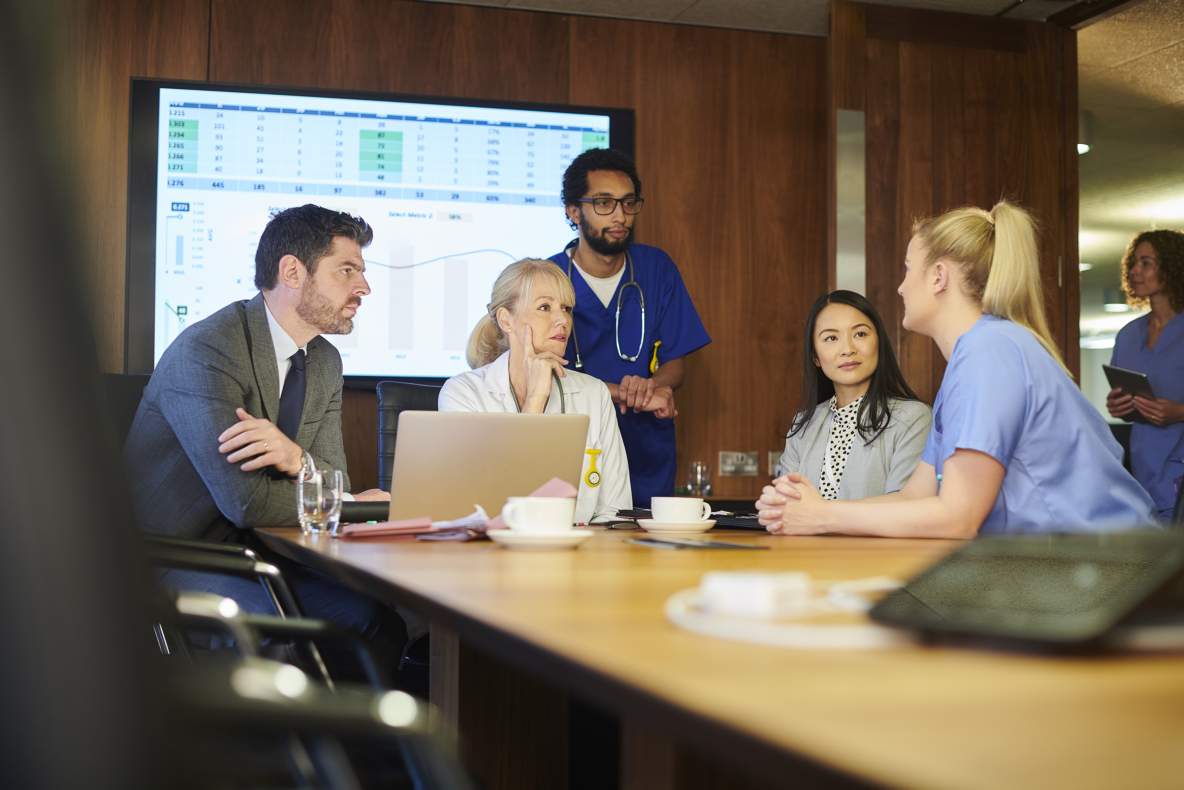 Vijf zorgprofessionals rond de tafel in overleg
