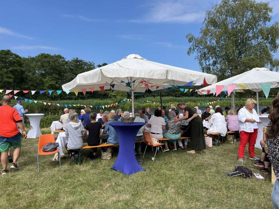 Inwoners van Wijdemeren aan picknicktafels onder parasols tijdens een buurtmaaltijd