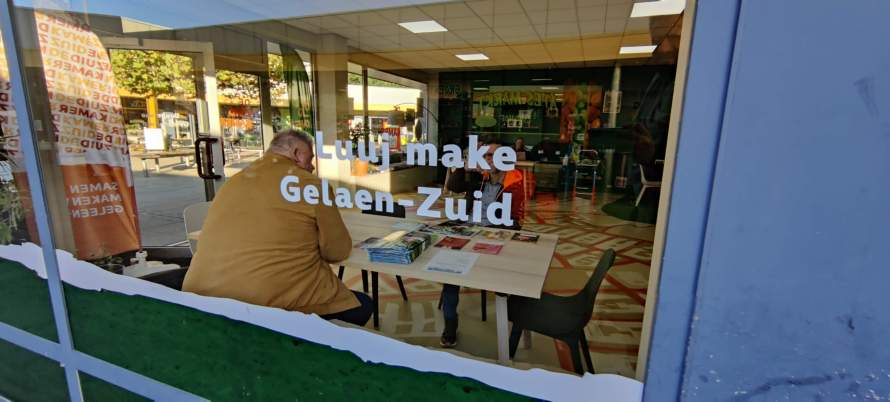 Een kijkje van buiten naar binnen bij de Zuidkamer. Een man zit aan een tafel de krant te lezen.