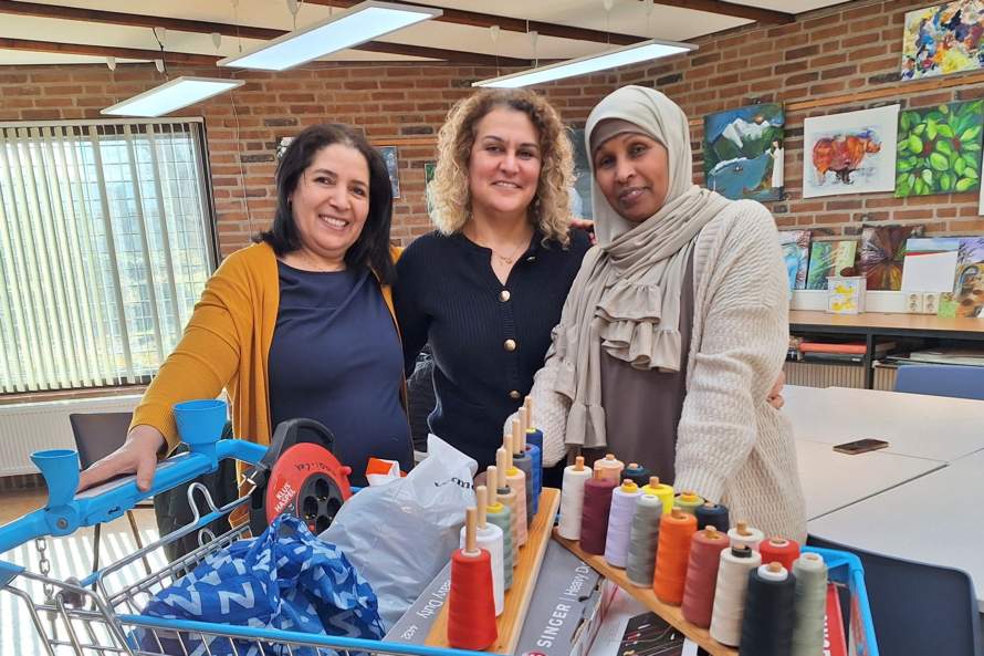 Drie vrouwen achter een winkelwagen met handwerkspullen en garenklossen